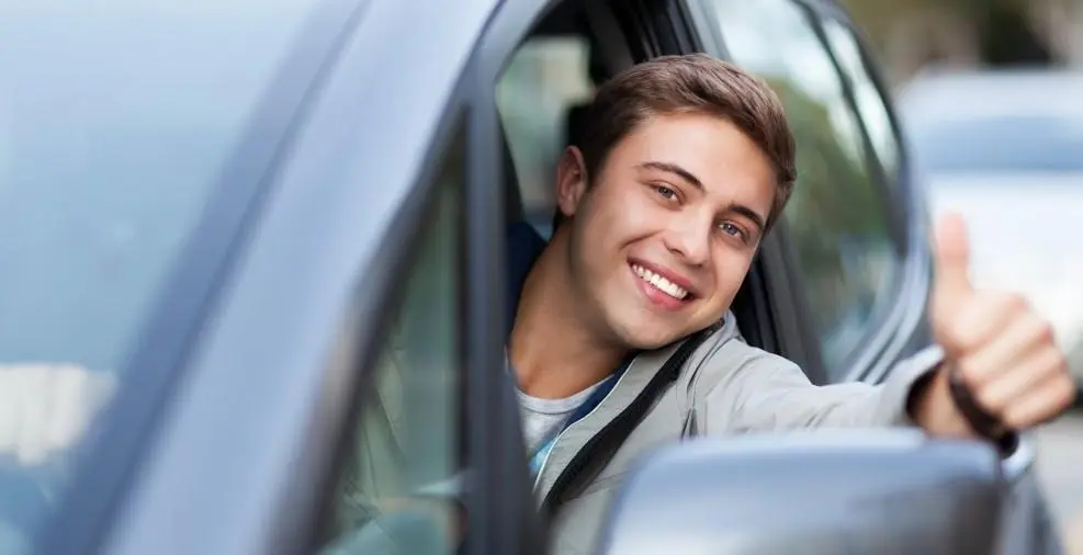 jovem branco de olhos claros faz sinal de joia com o polegar para fora do carro alugado com cnh provisória