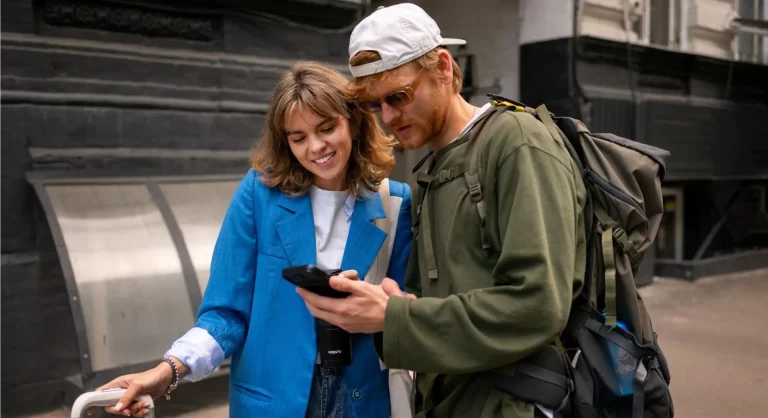 um homem e uma mulher parados olhando o celular e procurando aplicativos de viagem