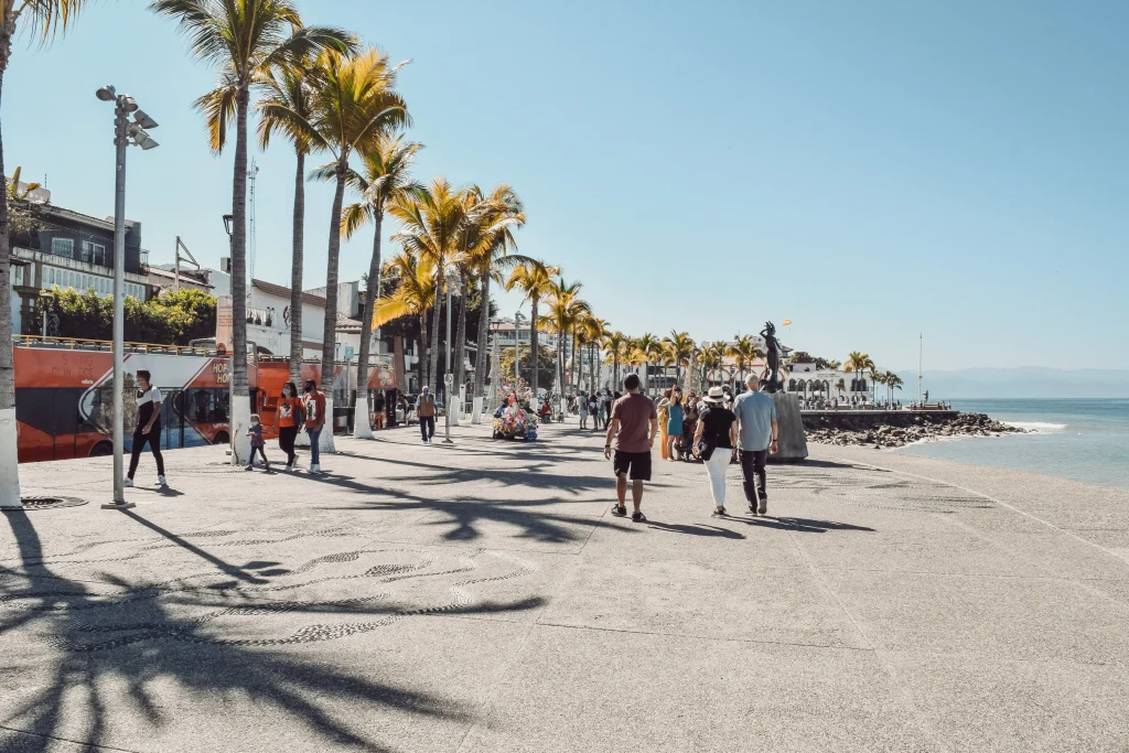 Foto de la gente caminando por una carretera de hormigón gris cerca del mar durante el día en Puerto Vallarta, una de las mejores playas de México.
