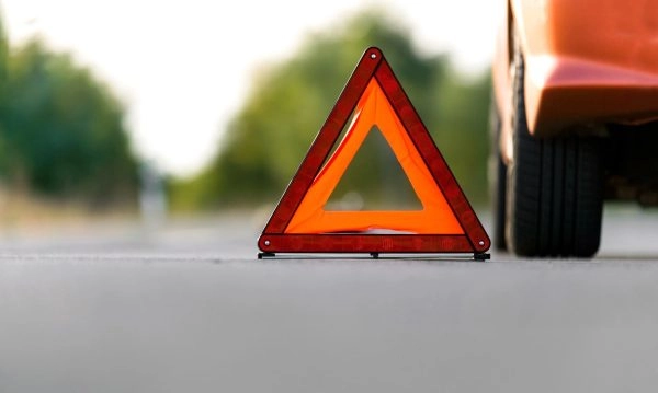 Image of a red car stopped on the road, with safety signage, waiting for car insurance