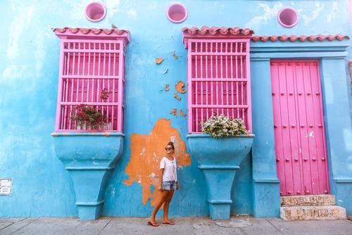 Uma mulher com casa colorida ao fundo.