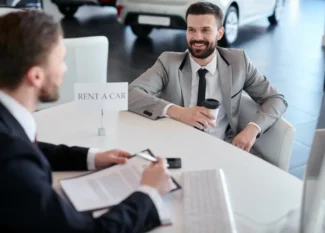 Two men in suits hold rental car documents at a car rental company.