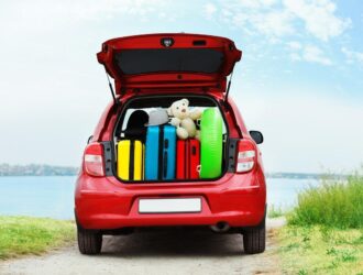 carro vermelho em uma praia com o porta malas aberto e cheio de malas coloridas