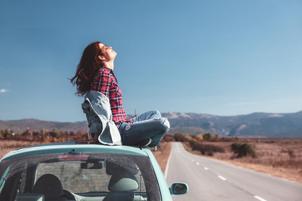 mulher sentada no teto do carro curtindo a paisagem da estrada