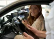 Mulher sorrindo dentro de um carro de aluguel mensal e do lado de fora o vendedor segura um tablet