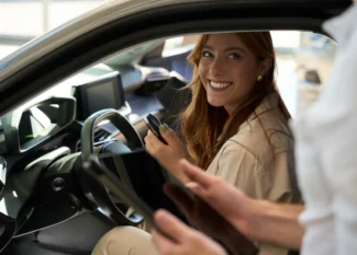 Mulher sorrindo dentro de um carro de aluguel mensal e do lado de fora o vendedor segura um tablet
