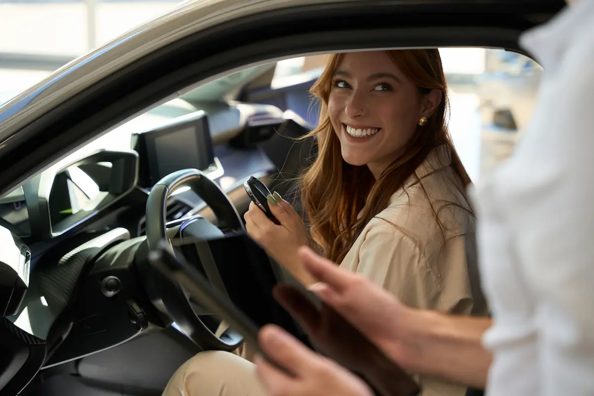 Mulher sorrindo dentro de um carro de aluguel mensal e do lado de fora o vendedor segura um tablet