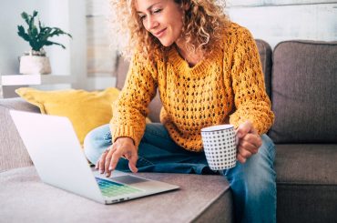 woman in yellow sweater with a mug in hand using a laptop