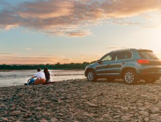 couple with dog by the lake with a car parked