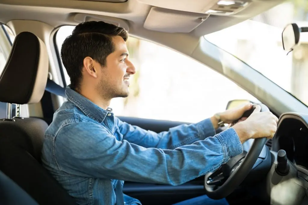 a man wearing a long sleve blue shirt driving a long term rental car