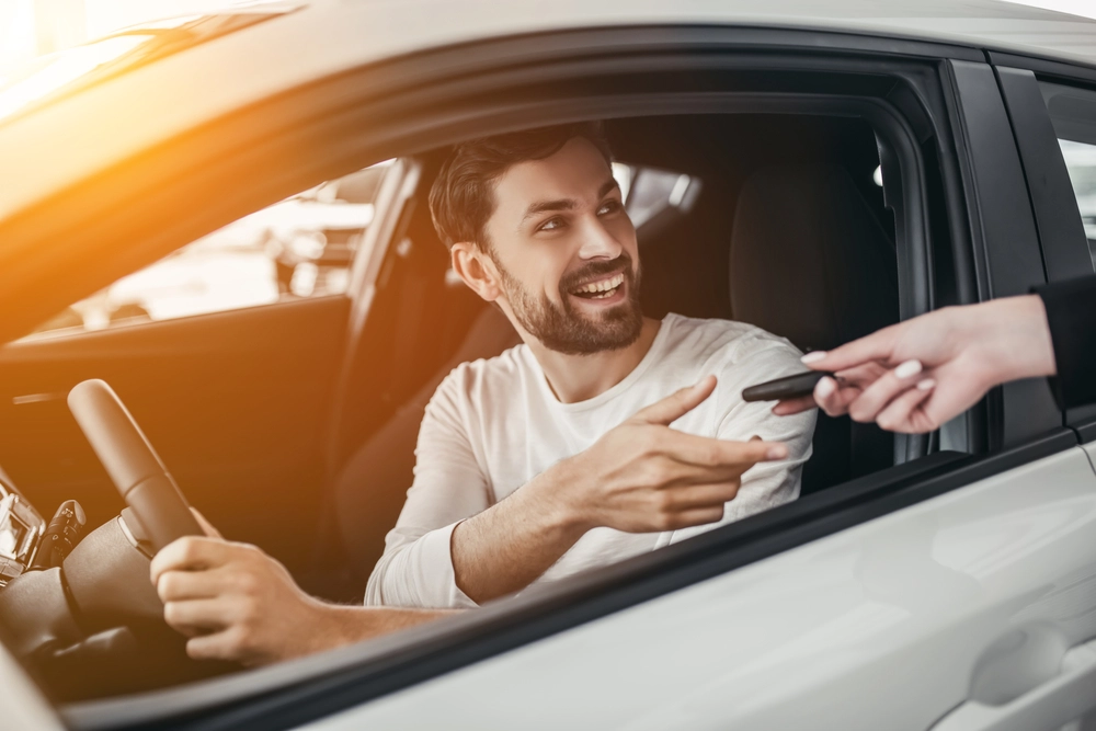 homem de camisa branca dentro de um carro devolvendo as chaves para pessoa ao lado de fora