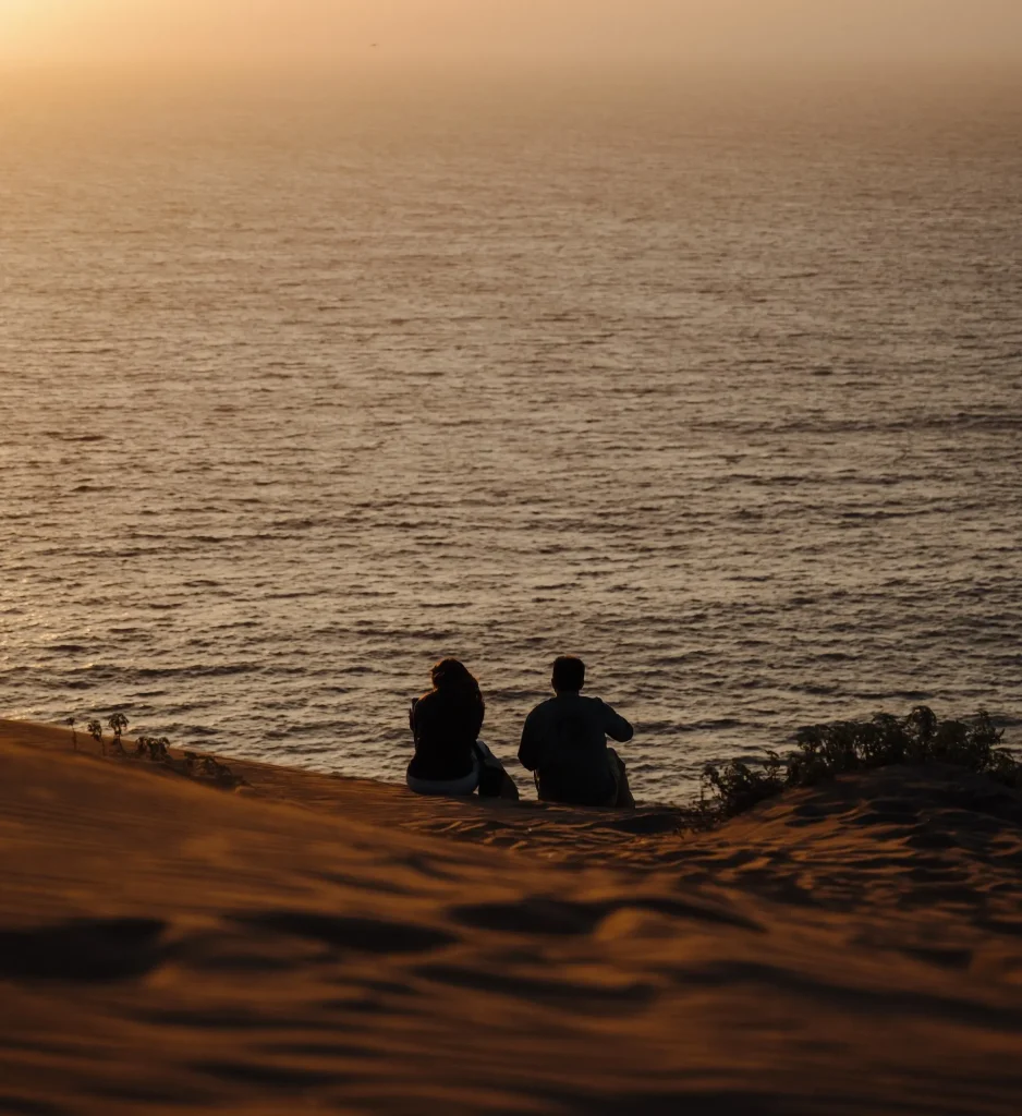 Foto de las dunas de Concón, uno de los destinos para escapada romántica en Chile, con vista al mar y dos personas de espaldas mirando al horizonte. 