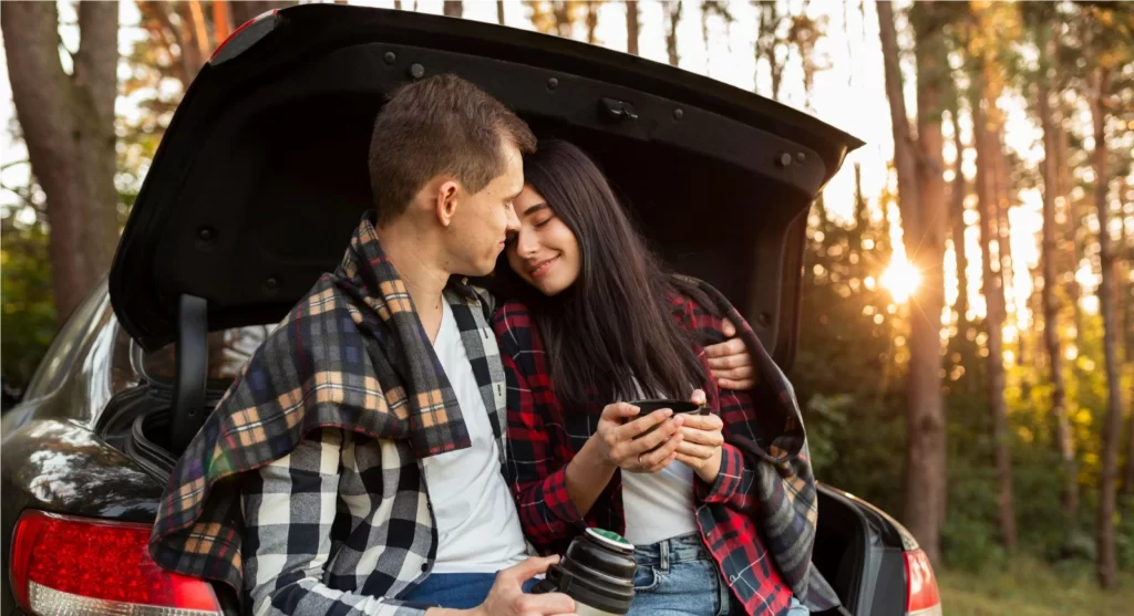 casal de homem e mulher sentados no porta malas aberto de um carro se abraçando