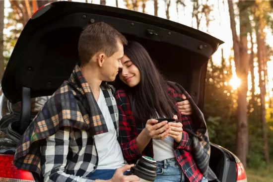 casal de homem e mulher sentados no porta malas aberto de um carro se abraçando