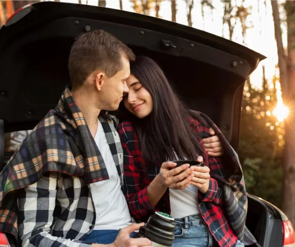 casal de homem e mulher sentados no porta malas aberto de um carro se abraçando