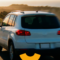 Vista traseira de um SUV azul em movimento na estrada de terra, com paisagem rural e luz do pôr do sol ao fundo, durante uma viagem