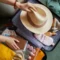 pessoa fazendo a mala de acordo com checklist de viagem guardando um chapéu de palha, cosméticos e passagens aéreas