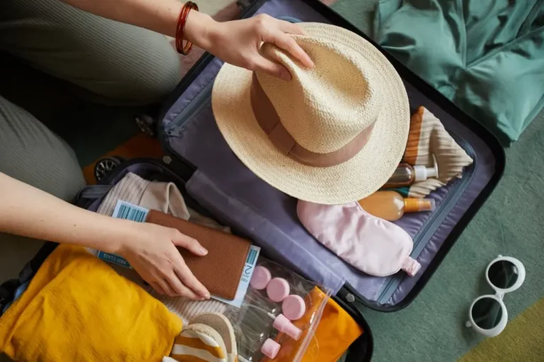 pessoa fazendo a mala de acordo com checklist de viagem guardando um chapéu de palha, cosméticos e passagens aéreas