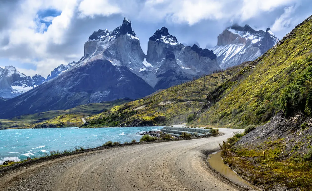 Foto da estrada dentro do Parque Nacional Torres del Paine no Chile, com as montanhas nevadas e o lago bem azul.
