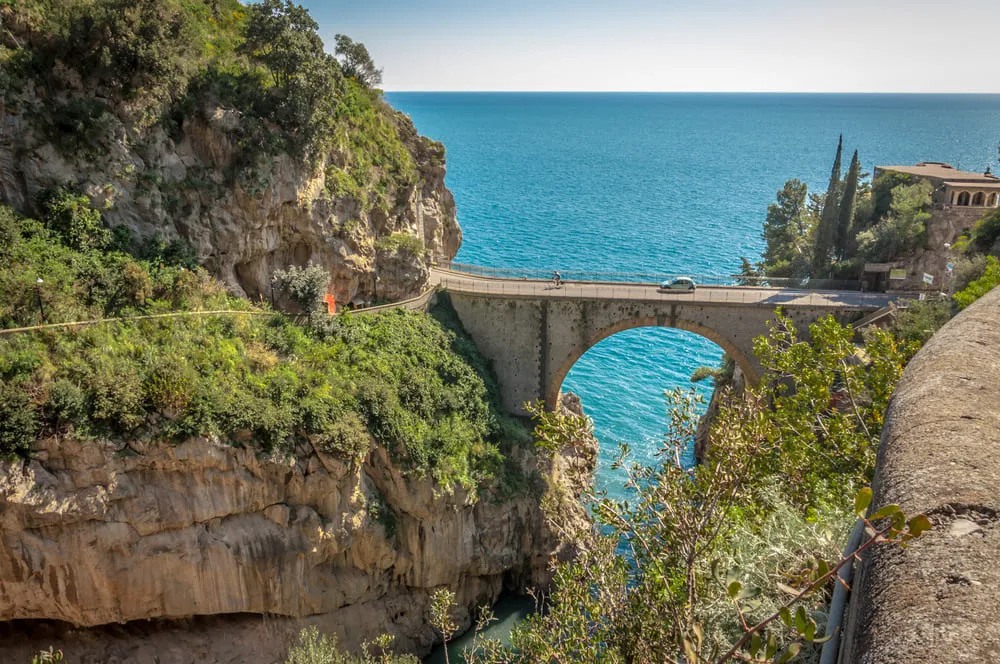 Foto incrível de uma estrada, onde passa um carro, na Costa Amalfitana, na Itália.