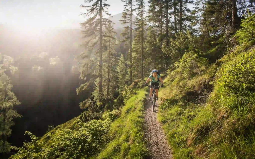 Mujer bajando una montaña con su bicicleta en un día soleado