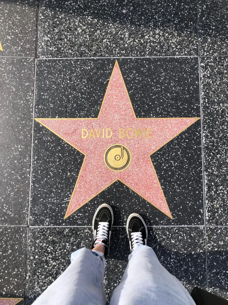Foto de uma das estrelas da Calçada da Fama, onde é possível ver o nome David Bowie. A estrela é rosa e o nome é escrito em dourado.
