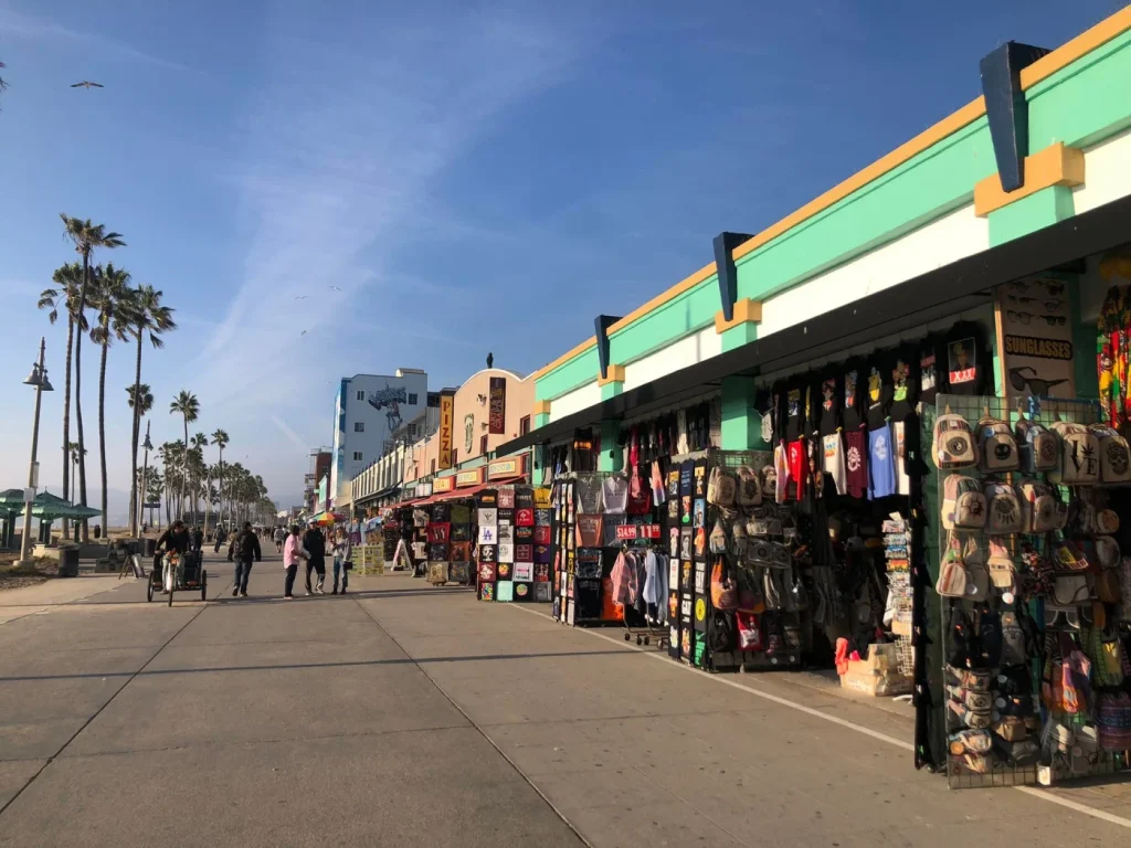 Foto das lojas de souvenires de Los Angeles na orla da Praia de Venice. O céu está bem azul. 