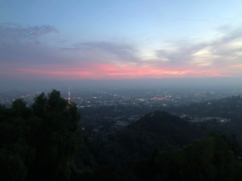 Vista da cidade de Los Angeles do alto do Griffith Observatory, o ponto mais alto de Los Angeles. As luzes da cidade estão acesas e o céu escurecendo.