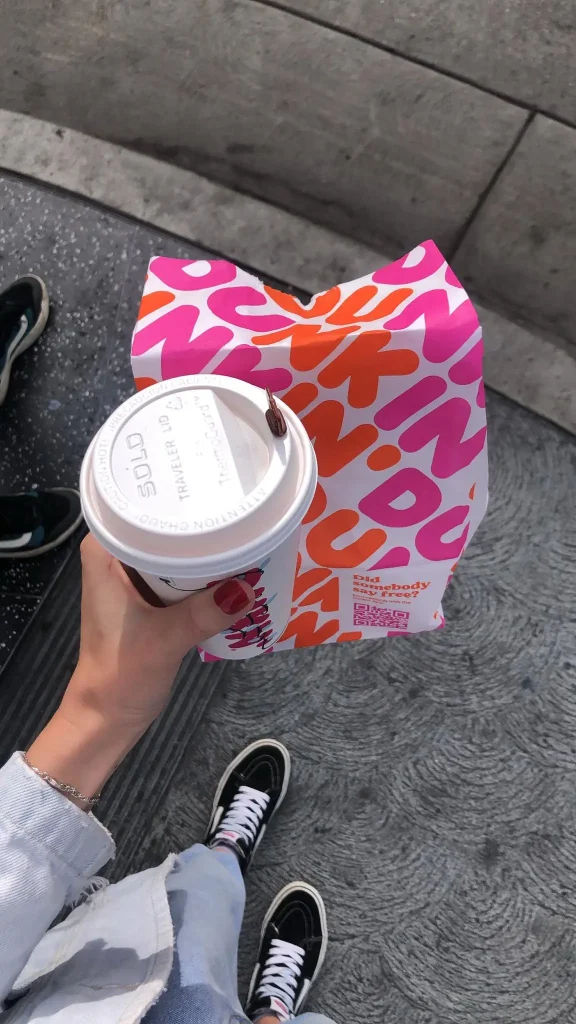 Foto de um café da manhã do Dunkin' Donuts, cafeteria famosa de Los Angeles. É possível ver o copo de café e uma sacola com donuts dentro.