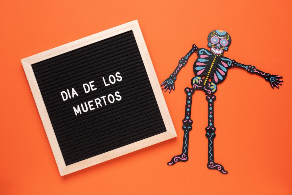 Imagen con un esqueleto y al lado escrito el día de los muertos con fondo negro