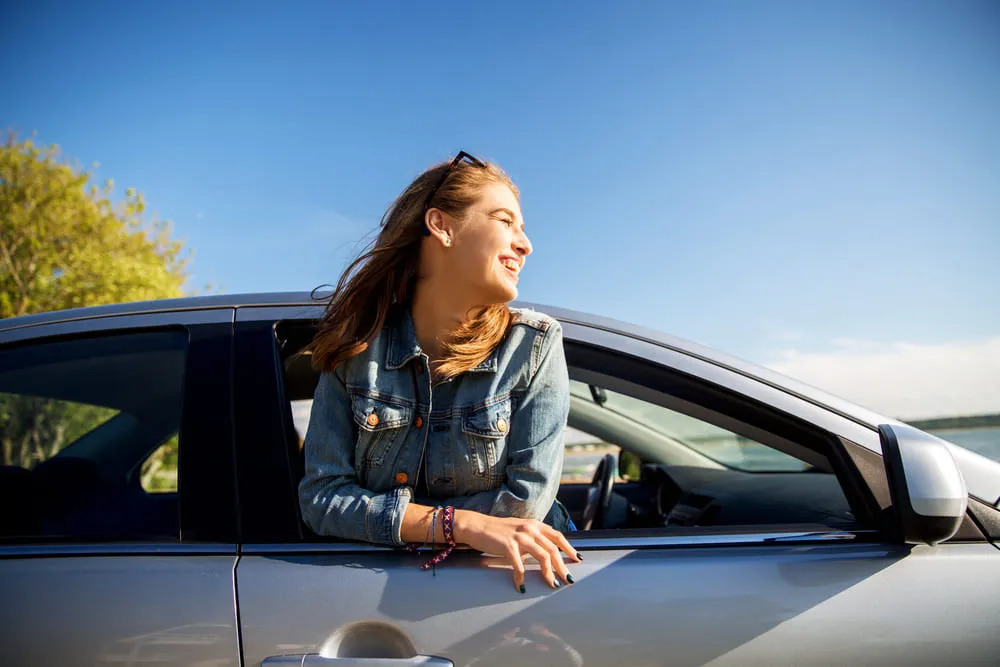 mulher com a metade do corpo para fora do carro com luz do sol no rosto