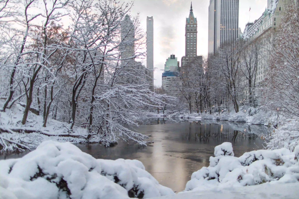 Paisaje nevado en Nueva york con un lago, un parque y el empire state building de fondo