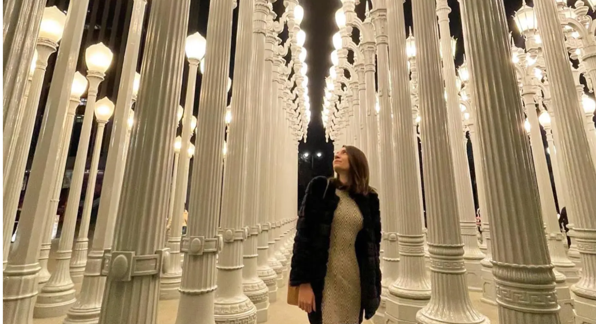 imagem de um salão com centenas de postes de luz brancos, com uma menina posando ao centro