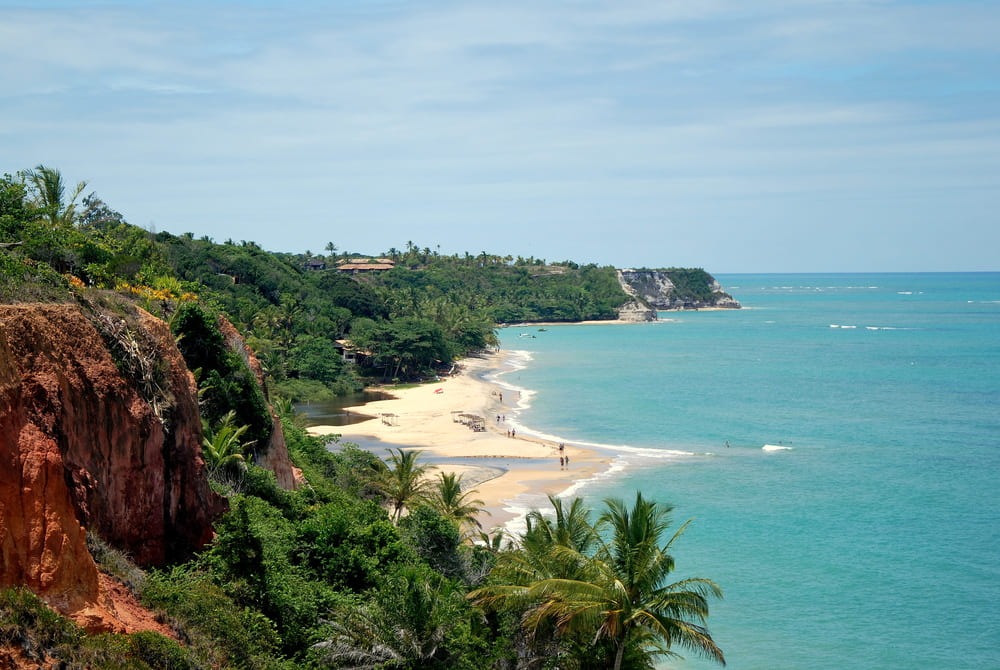 Foto de uma das praias encantadoras de Trancoso, na Bahia. O mar é bem azul e a vegetação bem verde.