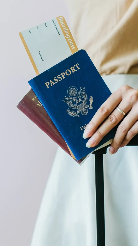 Foto de uma mão feminina segurando os documentos pessoais de viagem, como o passaporte, o visto e a passagem aérea.