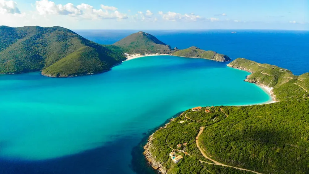 Foto aérea de Arraial do Cabo no Rio de Janeiro. O mar é bem azul com a vegetação verde em volta.