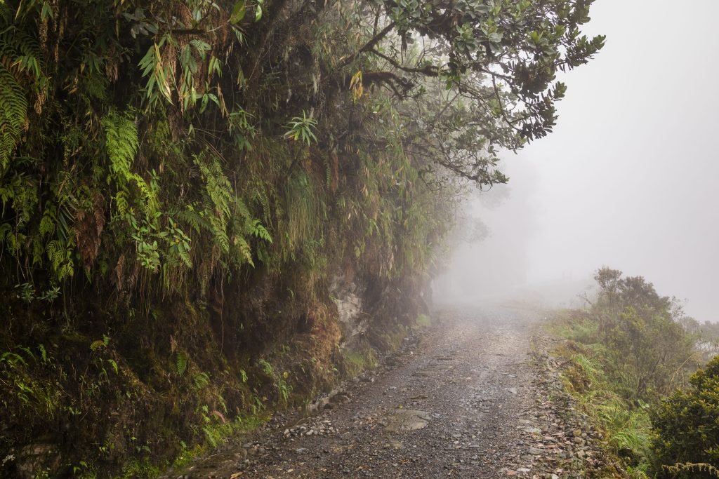 Foto da estrada Yungas, na Bolívia. A imagem mostra a neblina tomando conta da pista, repleta de pedras, tendo bem pouca visibilidade do que vem pela frente.