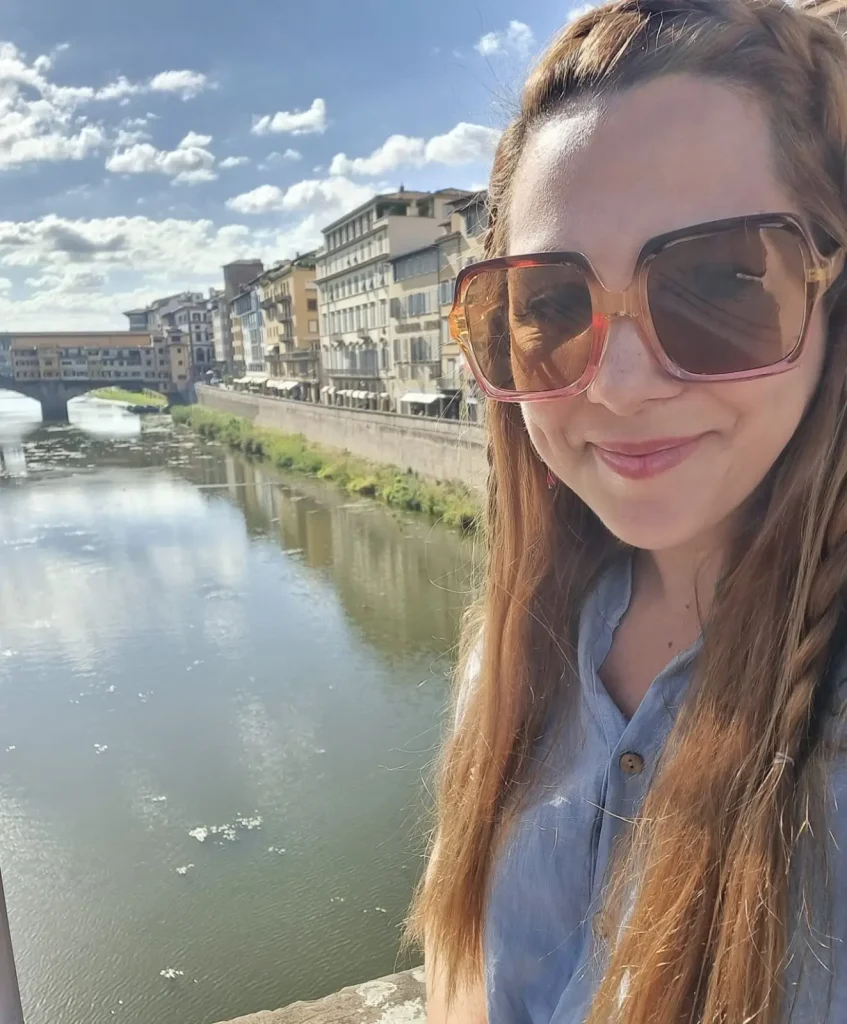Selfie de mujer de gafas sonriendo con el paisaje de un río detrás. 