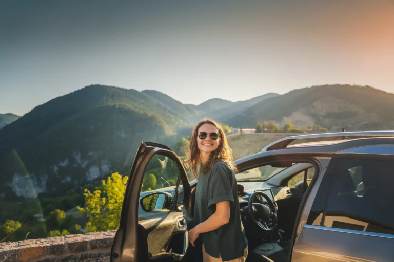 Foto de mujer en un mirador al lado de un carro abierto y con montañas en el paisaje.