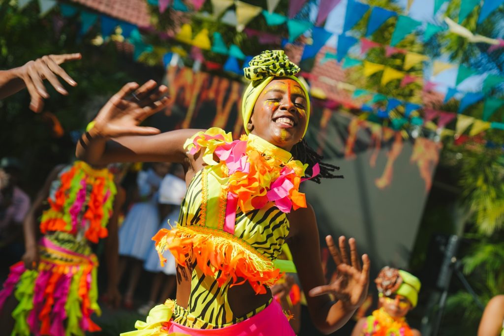 Bailarina del Carnaval de Barranquilla con un traje vibrante en tonos amarillo, naranja y rosa, sonriendo y danzando bajo banderines de colores.