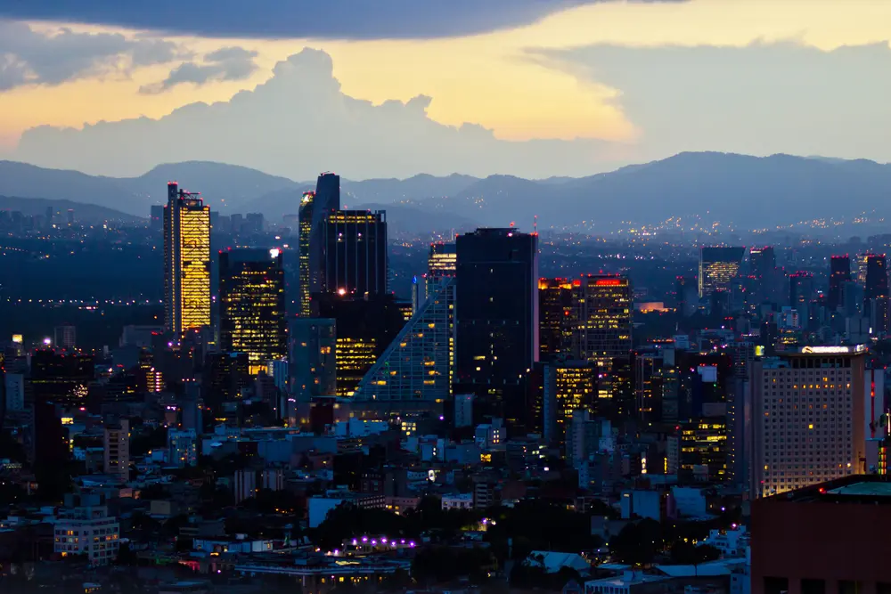 Foto del horizonte en Ciudad de México con muchos edificios, luces nocturnas y el cielo casi sin sol. 
