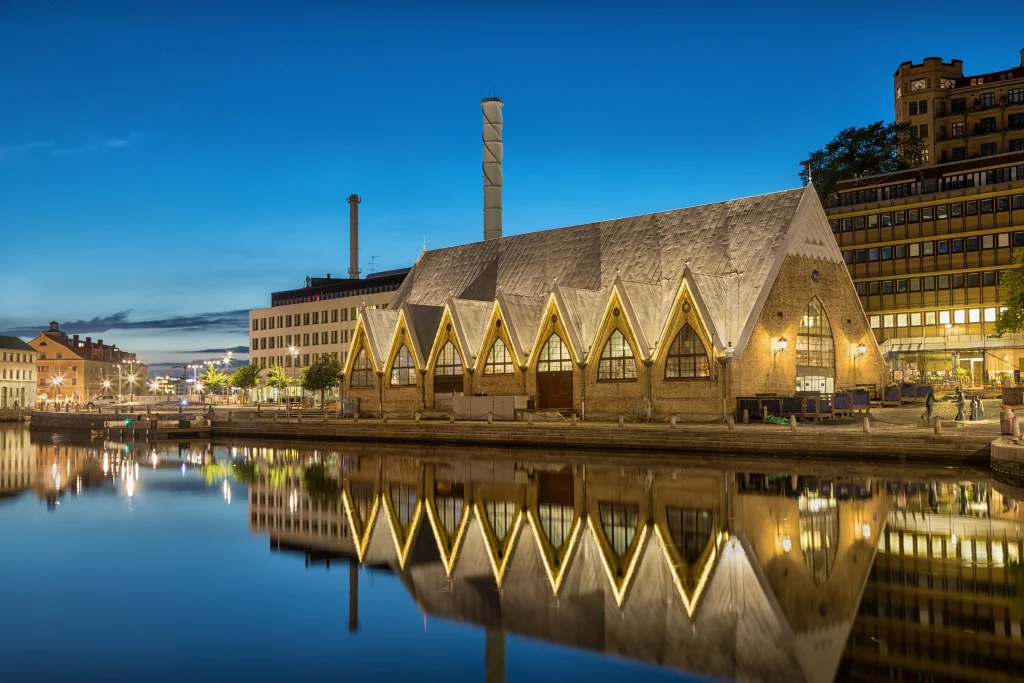Foto de uma construção imponente de Gotemburgo, na Suécia. O céu está super azul e a construção é refletida no lago ao lado.