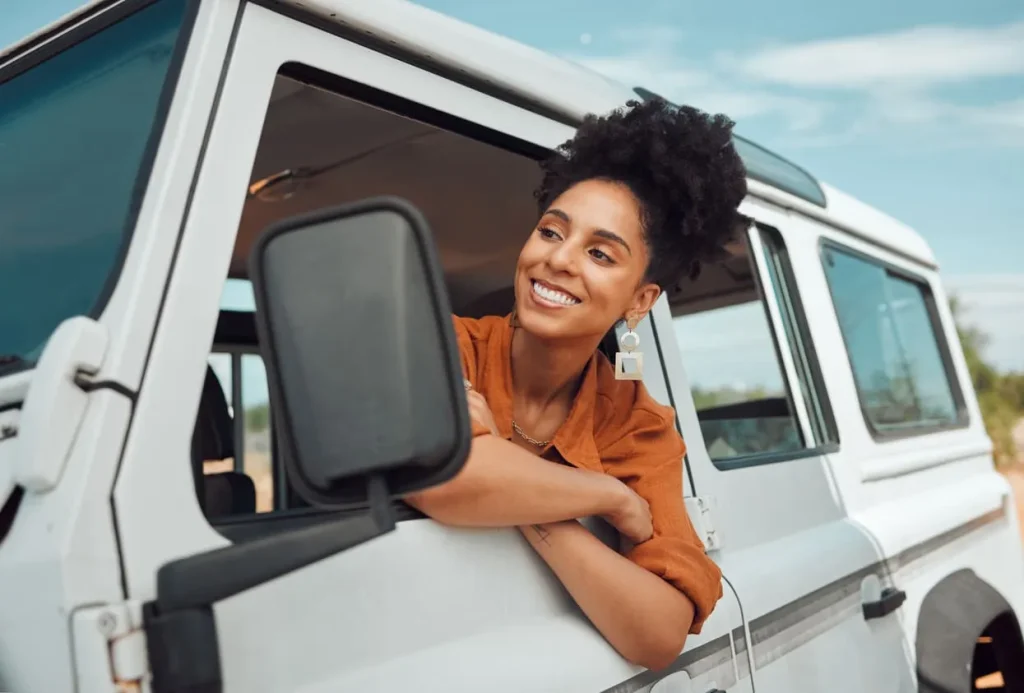 Foto de uma pessoa sorrindo na janela de um carro estacionado.