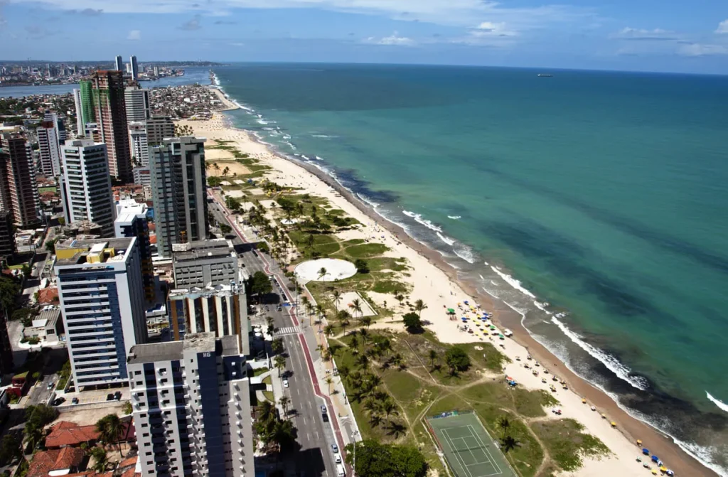 Foto da orla de Recife, em Pernambuco. O mar é super azul e tem uma infinidade de prédios residenciais e comerciais a beira do mar.