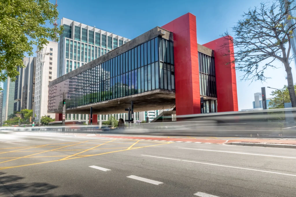 Foto do MASP, Museu de Arte de São Paulo, na capital paulista. A construção é futurística, com duas grandes sustentações na cor vermelha e todo o prédio é preenchido com vidros. A avenida Paulista está vazia.