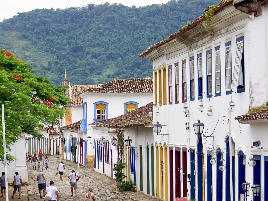 Foto das casas coloridas e famosas de Paraty no Rio de Janeiro. Há pessoas na rua que é feita de pedras.
