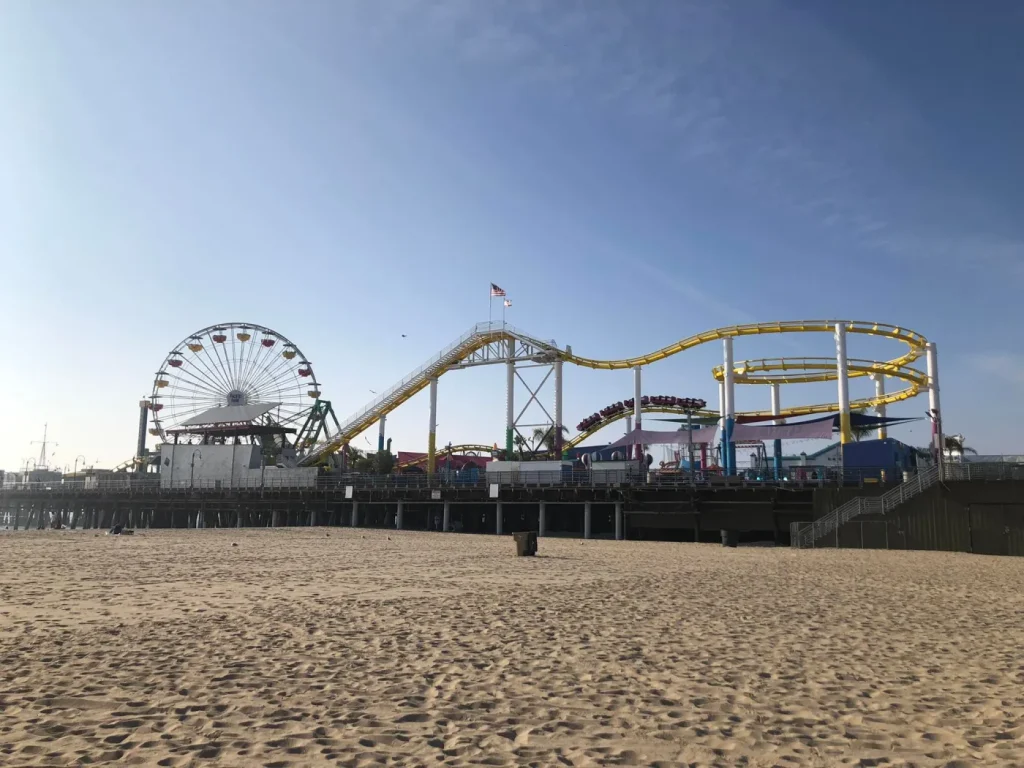 A wide view of the Santa Monica Pier, with the Pacific Park amusement rides and Ferris wheel visible in the distance.