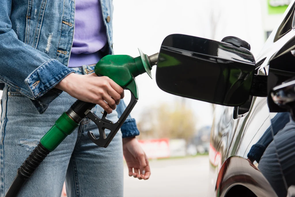 Uma mão feminina está segundo uma bomba de gasolina verde e abastecendo um carro preto.