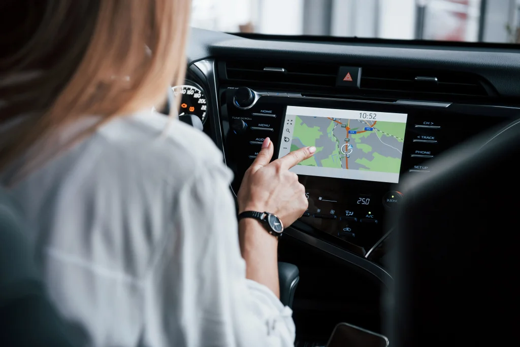 Uma mulher de costas está manuseando um GPS que está dentro de um carro no painel de controle.