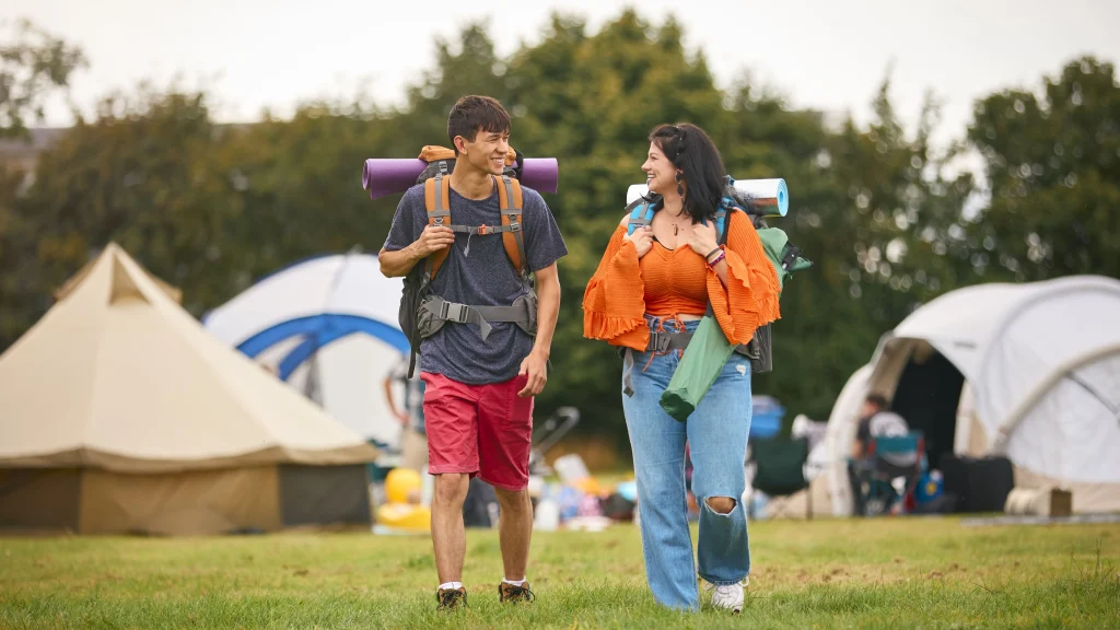 Um homem e uma mulher se olhando ao caminhar entre barracas em um festival de música e carregar suas mochilas de acampamento.